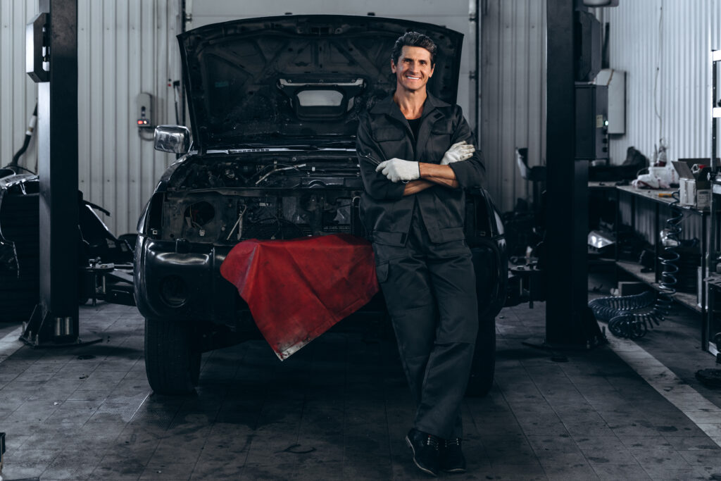 auto mechanic standing in repair shop inspecting vehicle engine for preventative maintenance to help cars reach 200k miles and improve long term reliability