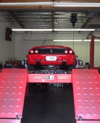Red Ferrari on a lift inside Airpark Auto Clinic service bay, showcasing Brake inspection
