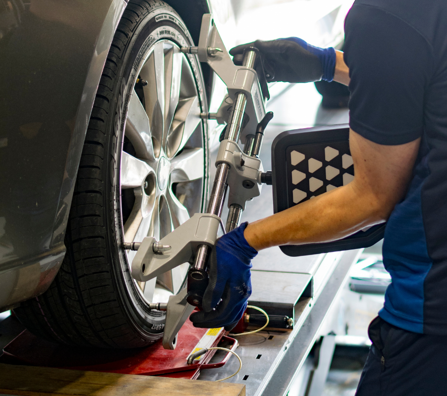 Technician adjusting wheel alignment equipment on car tire, highlighting the importance of proper alignment for safety and tire longevity.